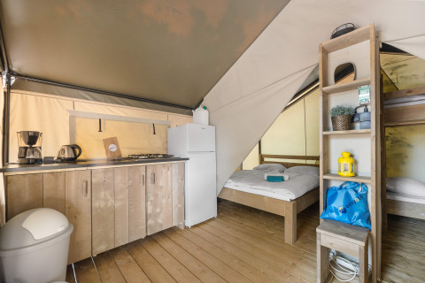 Interieur van een safaritent met keuken, tweepersoonsbed, stapelbed en houten vloer.