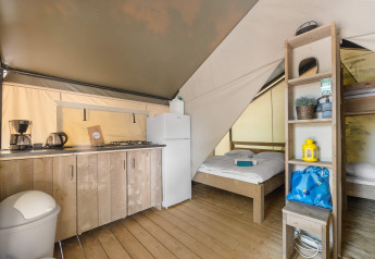 Binnenkant van een safaritent met keukentje, tweepersoonsbed, stapelbed en houten vloer.