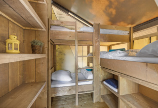 Interno di tenda safari con letti a castello in legno e scaffali, ideale per un'esperienza famigliare.