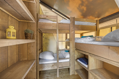 Interieur van safaritent met houten stapelbedden en planken, ideaal voor een avontuurlijke familievakantie.