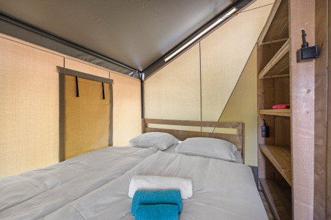Gemütliches Schlafzimmer in einem Safarizelt mit Doppelbett, Bettwäsche, Handtüchern und Holzregalen.