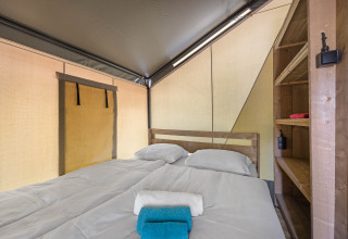 Knusse slaapkamer in een safaritent met tweepersoonsbed, schone handdoeken en houten opbergrekken.