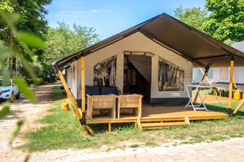 Safari Tent Comfort mit Holzveranda, Outdoor-Sitzgelegenheiten und grüne Umgebung bei sonnigem Wetter