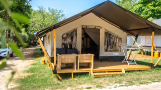 Safari Tent Comfort con terraza de madera, asientos exteriores y vegetación bajo un cielo soleado