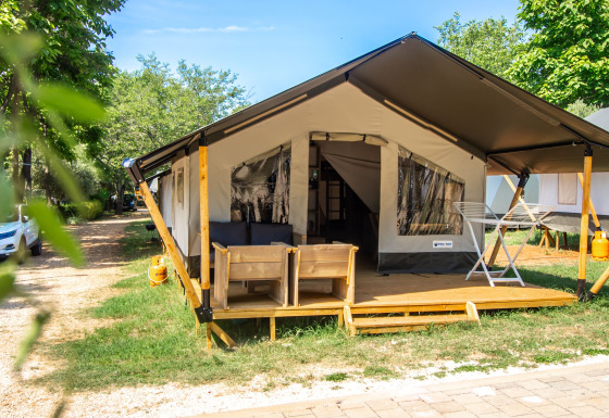 Safari Tent Comfort con terraza de madera, asientos exteriores y vegetación bajo un cielo soleado