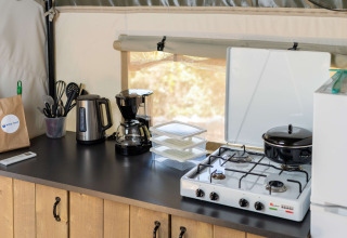 Keukenhoek in safaritent met waterkoker, koffiezetapparaat, gasfornuis, pannen, gerei en bakjes.