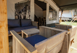 Zona de estar exterior en tienda safari, con muebles de madera y cojines azules, vista al interior.