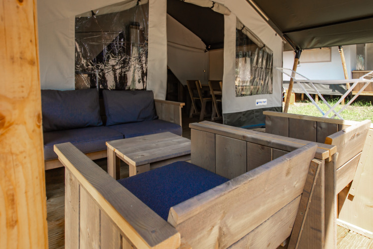 Outdoor seating area in a safari tent, featuring wooden furniture with blue cushions and a view inside.