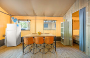Intérieur d'une tente safari avec plancher en bois, table à manger, quatre chaises, réfrigérateur et chambre.