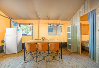 Interno di una tenda safari con pavimento in legno, tavolo da pranzo, quattro sedie e frigorifero.