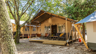 Tenda Safari Lodge con aria condizionata, veranda esterna, comode sedute e alberi in un ambiente naturale.