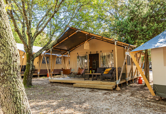 Safari tent Lodge met airco en terras met zitplaatsen, omgeven door bomen in een groene, rustige omgeving.