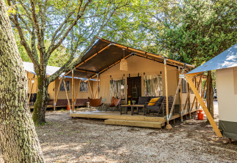Safari tent Lodge with air conditioning, outdoor deck, cozy seating and trees in a serene forest setting.