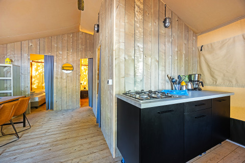Interior de tienda safari con cocina moderna, suelo de madera y acceso a dormitorios con cortinas.