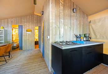 Interieur van een safaritent met een moderne kitchenette en houten vloer, slaapkamers achter gordijnen.