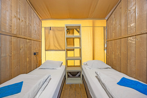 Deux lits simples et une étagère dans une tente safari en bois au Camping Lanterna en Croatie, bien éclairé.