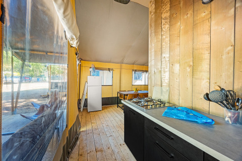 Innenaufnahme eines Safari Lodge-Zeltes mit Klimaanlage, sichtbar sind Küche, Esstisch und Kühlschrank.