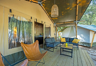 Safari tent terras met gezellige zithoek, vlinderstoel en lantaarn, gelegen in een bosrijke omgeving.