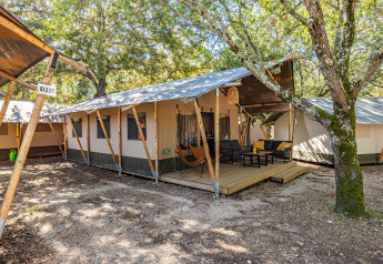 Vista esterna di una tenda Safari Lodge con aria condizionata, veranda in legno e zona relax tra gli alberi.