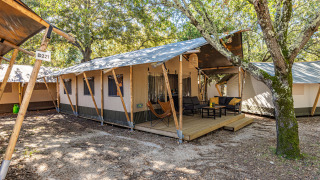 Outdoor view of a Safari tent Lodge with air conditioning, wooden deck, and seating surrounded by trees.