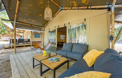 Outdoor seating area of a safari tent with sofas, tables, and a view of other tented accommodations.