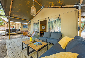 Gemütlicher Außenbereich eines Safari-Zeltes mit Sofas, Tischen und Blick auf weitere Zelte.