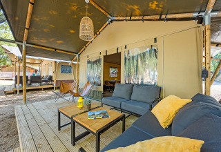 Outdoor seating area of a safari tent with sofas, tables, and a view of other tented accommodations.