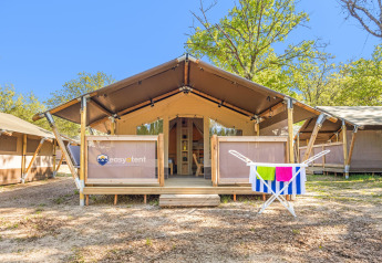 Tenda safari Lodge con aria condizionata, circondata da alberi, asciugamani colorati appesi all'esterno.