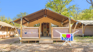Safari tent Lodge with air conditioning, wooden deck, trees in background, towels hanging outside.