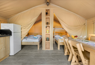 Interior de una tienda safari con cama doble, literas, cocina, nevera y mesa de comedor.