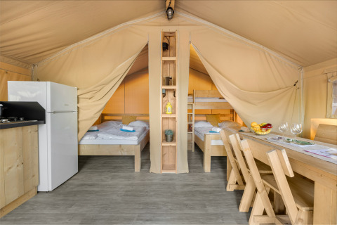 Interieur van een safaritent met tweepersoonsbed, stapelbedden, keuken, koelkast en eettafel.
