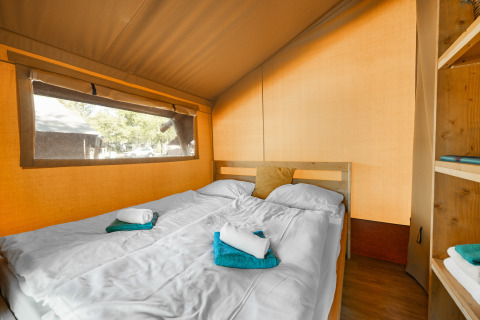 Innenansicht eines Safarizeltes mit Doppelbett, frischen Handtüchern und großem Fenster zur Natur.