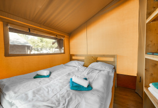 Intérieur d’une tente safari avec lit double, serviettes fraîches et grande fenêtre donnant sur la nature.