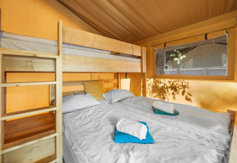 Vista interna di una tenda safari con letto matrimoniale, letto a castello, finestra e asciugamani piegati.