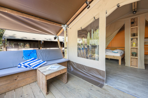 Tienda safari con acogedora zona de estar exterior, muebles de madera y vista al dormitorio interior.
