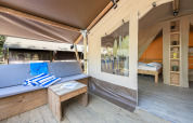 Safari tent featuring a cozy outdoor lounge with wooden furniture and view into the bedroom with a bed.