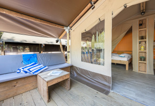 Tienda safari con acogedora zona de estar exterior, muebles de madera y vista al dormitorio interior.