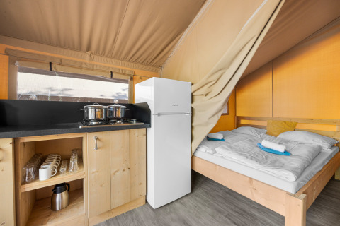 Innenansicht eines Safarizeltes mit Küchenzeile, Kühlschrank und Doppelbett mit Handtüchern.