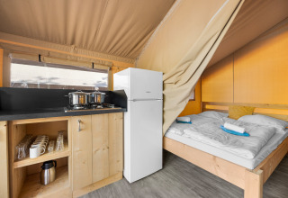 Interieur van een safaritent met kitchenette, koelkast en tweepersoonsbed met opgevouwen handdoeken.