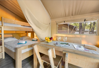 Vista interna di una tenda safari con letto a castello, tavolo da pranzo, fruttiera e finestra panoramica.