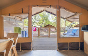 Interior view from a safari tent with open panels, wooden deck outside, and seating area in the sun.