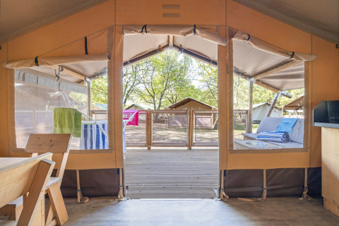 Interior view from a safari tent with open panels, wooden deck outside, and seating area in the sun.