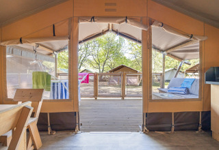 Interior view from a safari tent with open panels, wooden deck outside, and seating area in the sun.
