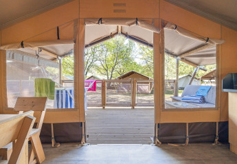 Vue intérieure depuis une tente safari avec panneaux ouverts, terrasse en bois et espace détente dehors.