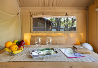 Dentro una tenda safari con cesta di frutta, due bicchieri da vino e fogli su tavolo di legno rustico.