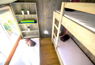 View of three single beds and a wooden shelf inside a bright safari tent at Camping Valkanela, Croatia.