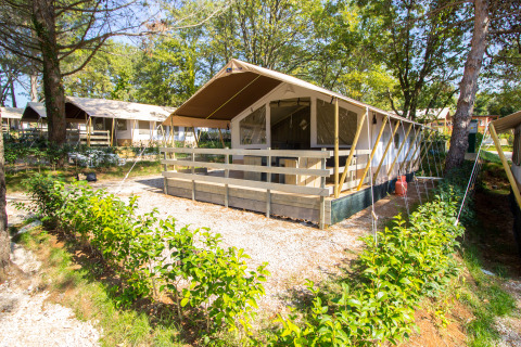 Tienda safari con instalaciones sanitarias en Camping Valkanela, Croacia, rodeada de árboles y vegetación.
