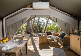 Binnenzicht van Safari tent Comfort met airco, eettafel en gezellige zithoek in een bosrijke omgeving.