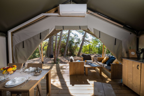 Interno della tenda Safari Comfort con aria condizionata, tavolo da pranzo e zona relax accogliente.