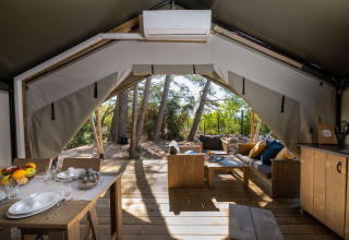 Binnenzicht van Safari tent Comfort met airco, eettafel en gezellige zithoek in een bosrijke omgeving.